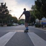 A skateboarder cruising into the street view from the back